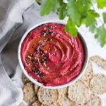 beet and white bean dip in bowl with crackers and parsley