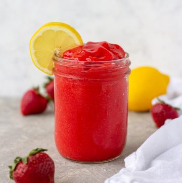 bright red strawberry slushie in a mason jar with a lemon round garnish