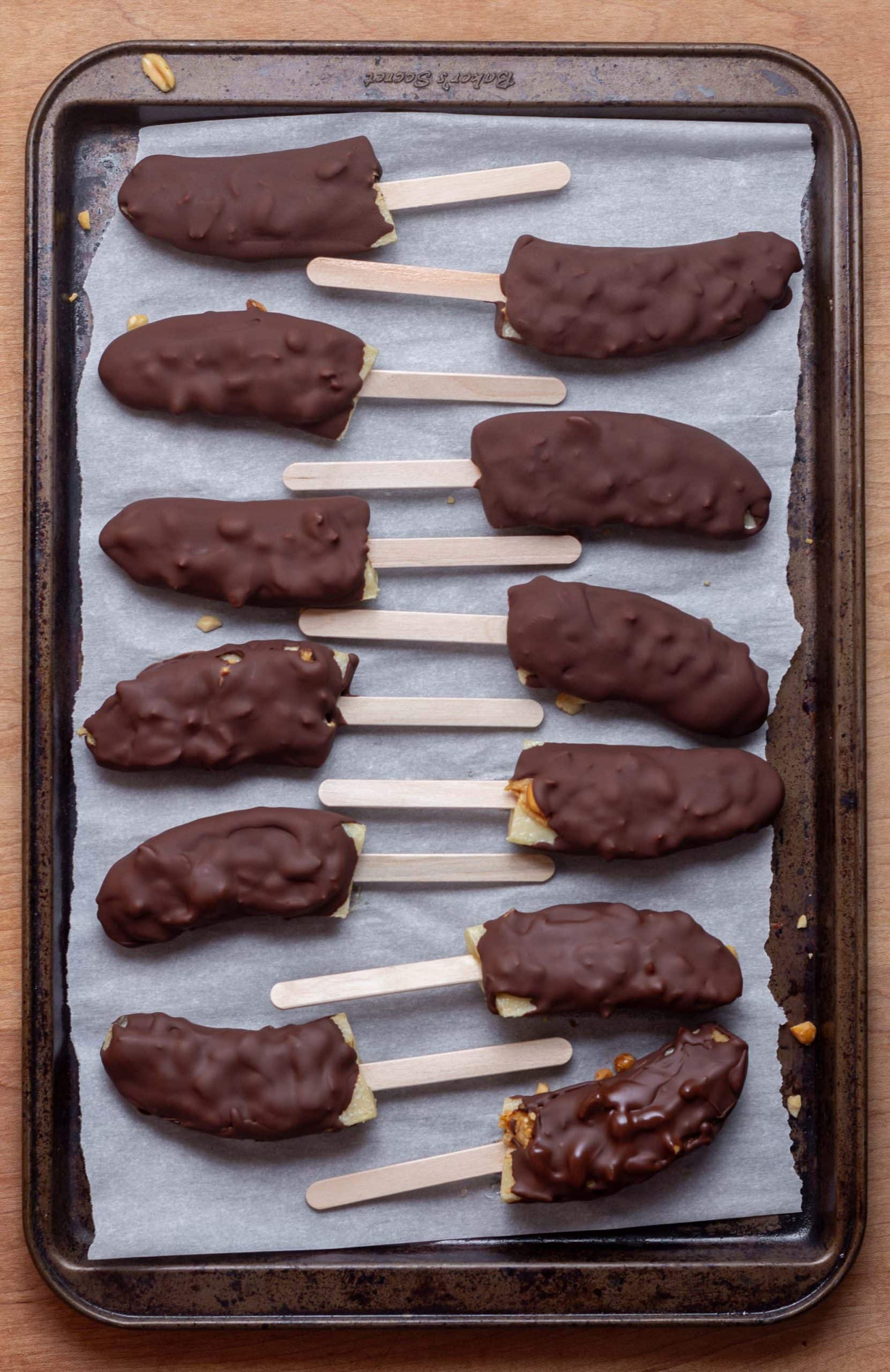 chocolate covered banana pops laying on a parchment paper lined baking tray
